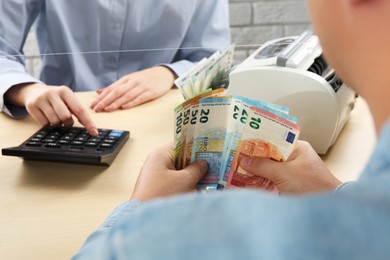 Photo of Client counting money at table in currency exchange, closeup