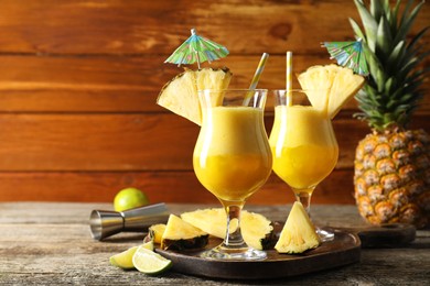 Photo of Tasty pineapple cocktail in glasses served on wooden table, space for text