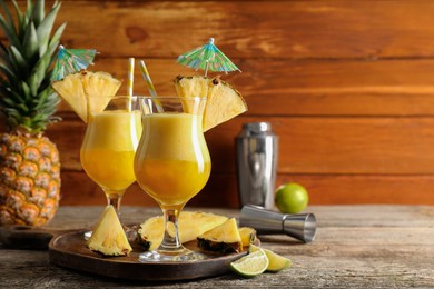 Photo of Tasty pineapple cocktail in glasses served on wooden table, space for text