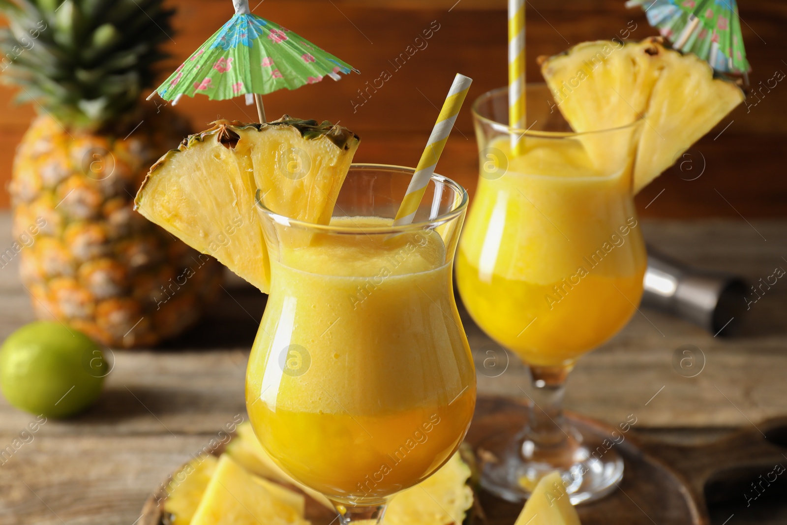 Photo of Tasty pineapple cocktail in glasses served on wooden table, closeup