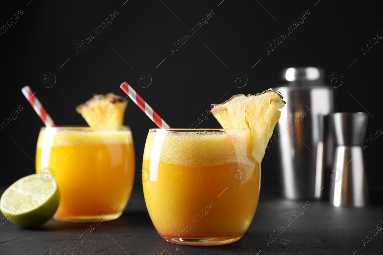 Photo of Tasty pineapple cocktail in glasses served on black table, closeup