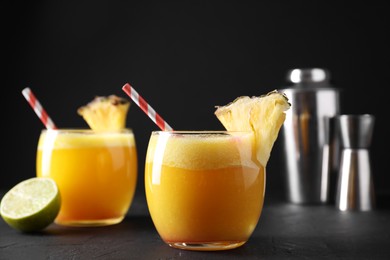 Photo of Tasty pineapple cocktail in glasses served on black table, closeup