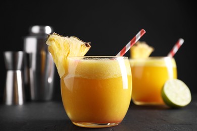 Photo of Tasty pineapple cocktail in glasses served on black table, closeup