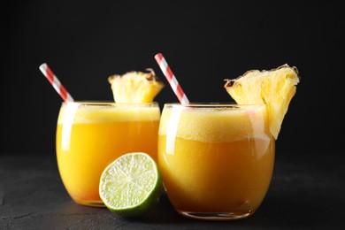 Photo of Tasty pineapple cocktail in glasses served on black table, closeup