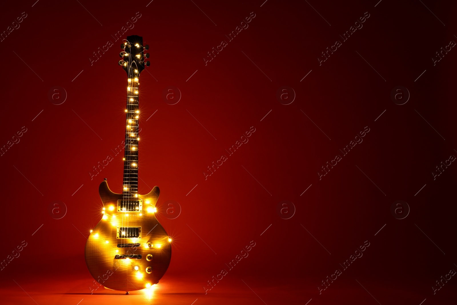 Photo of Electric guitar with Christmas lights on dark red background. Space for text