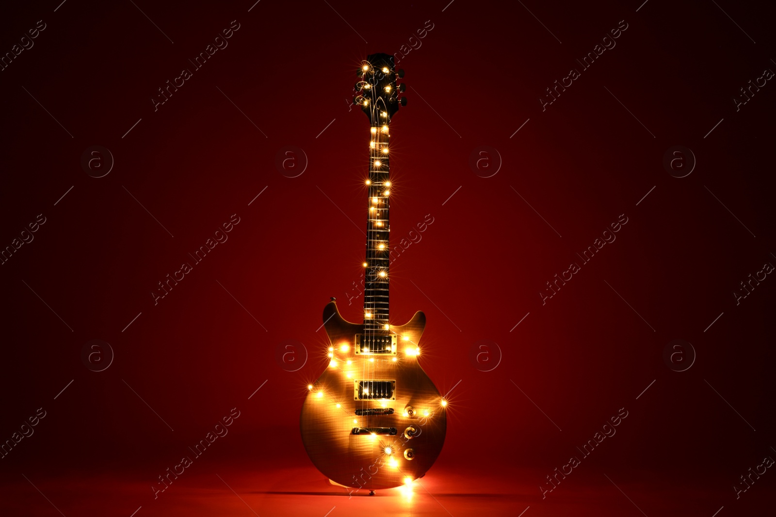 Photo of Electric guitar with Christmas lights on dark red background