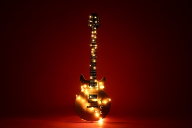 Photo of Electric guitar with Christmas lights on dark red background