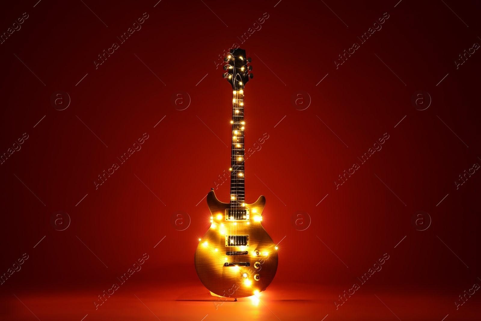 Photo of Electric guitar with Christmas lights on dark red background