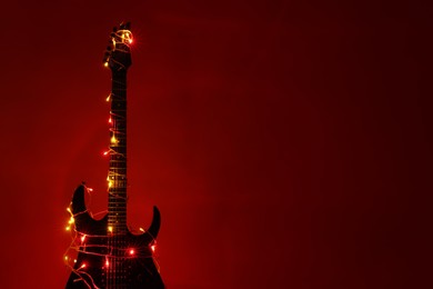 Photo of Electric guitar with Christmas lights on dark red background. Space for text