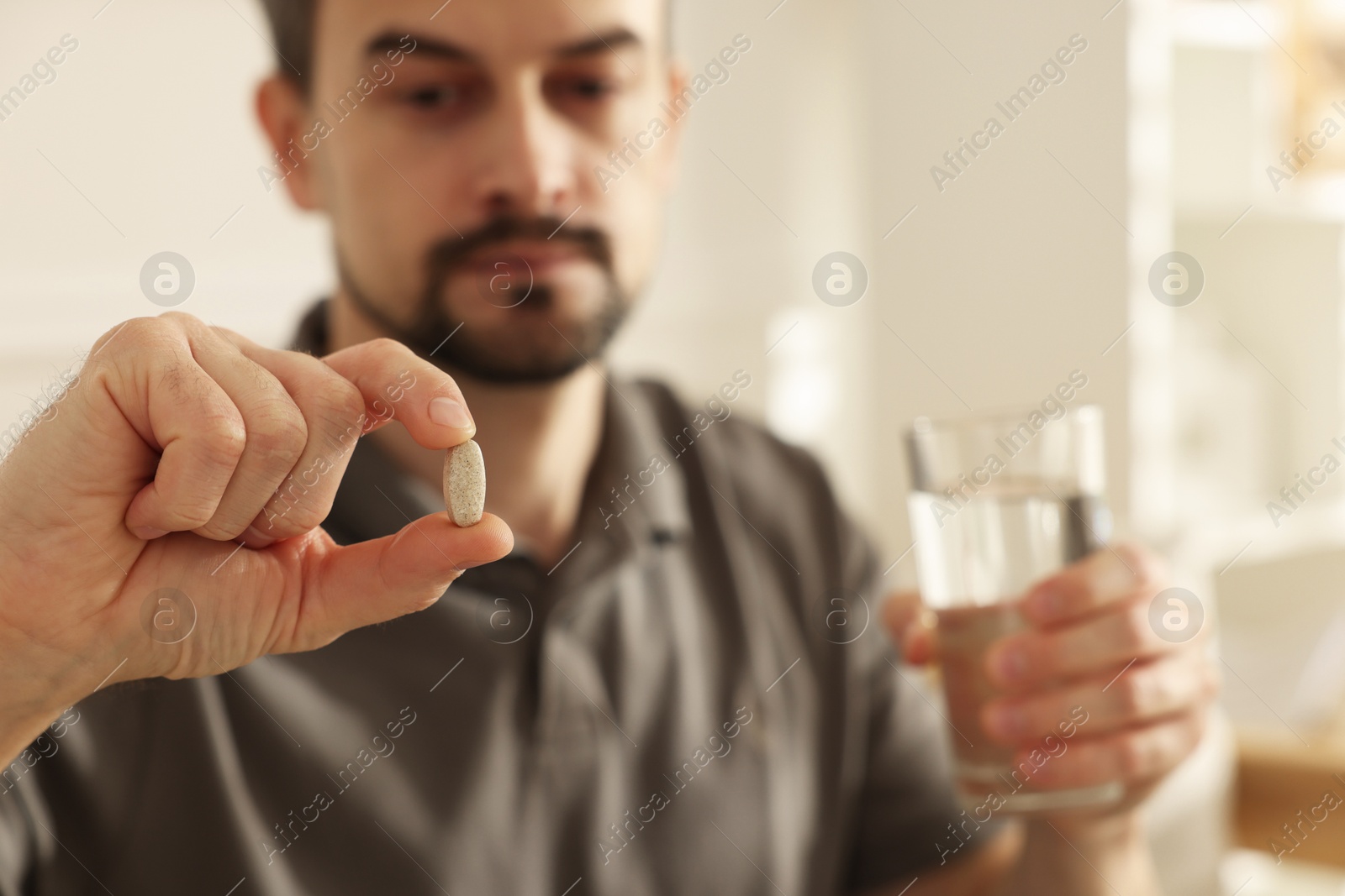 Photo of Man with pill and glass of water at home, selective focus