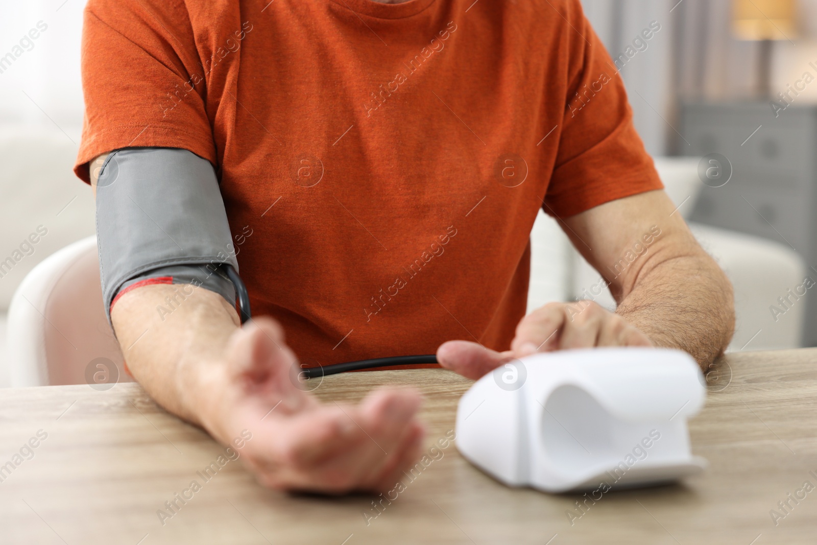 Photo of Senior man measuring blood pressure at table indoors, closeup