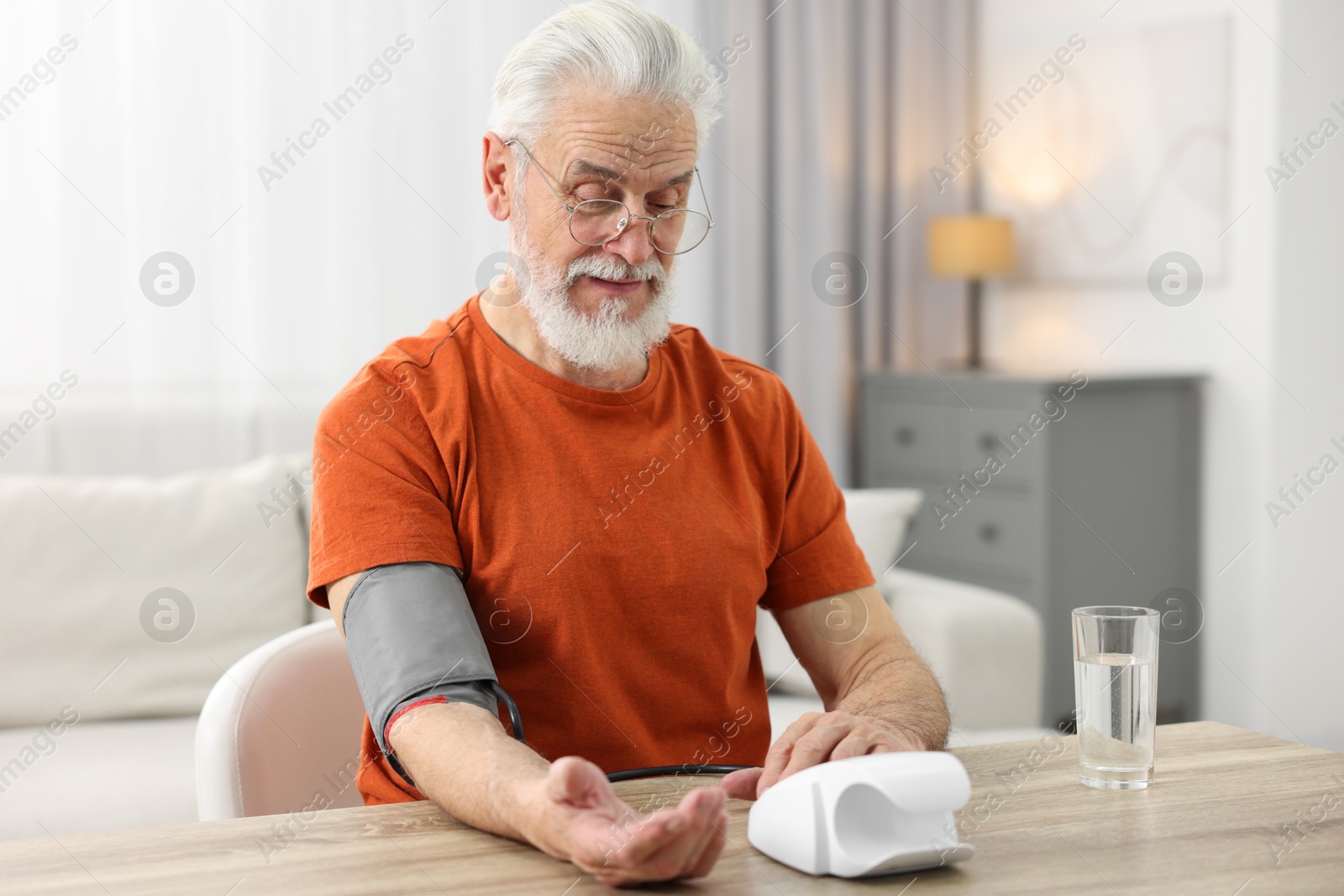 Photo of Senior man measuring blood pressure at table indoors