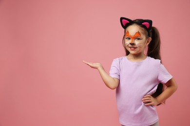 Cute girl with painted face and ears as cat on pink background, space for text