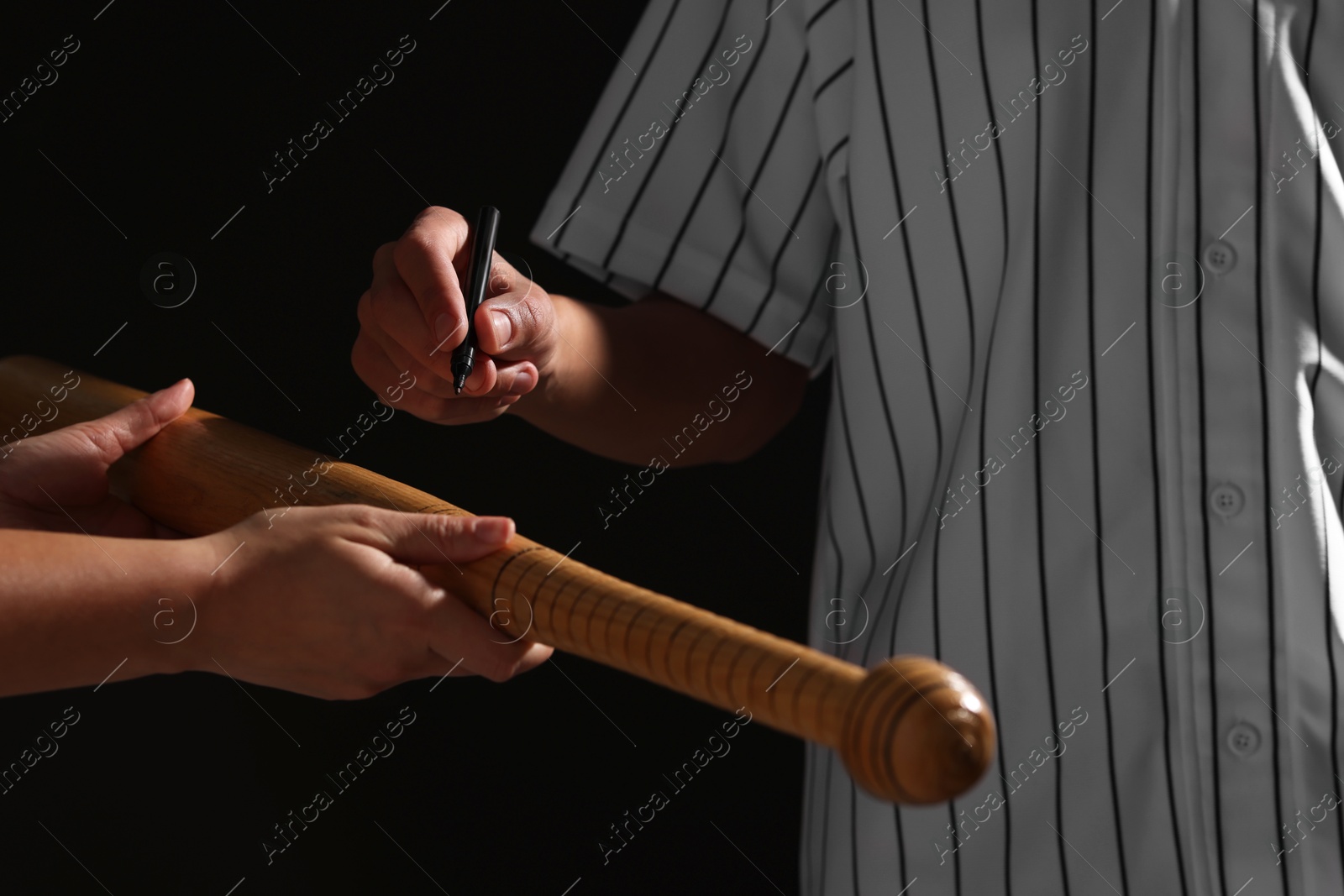 Photo of Baseball player signing autograph on bat against black background, closeup