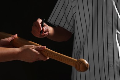 Photo of Baseball player signing autograph on bat against black background, closeup