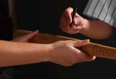 Photo of Baseball player signing autograph on bat against black background, closeup