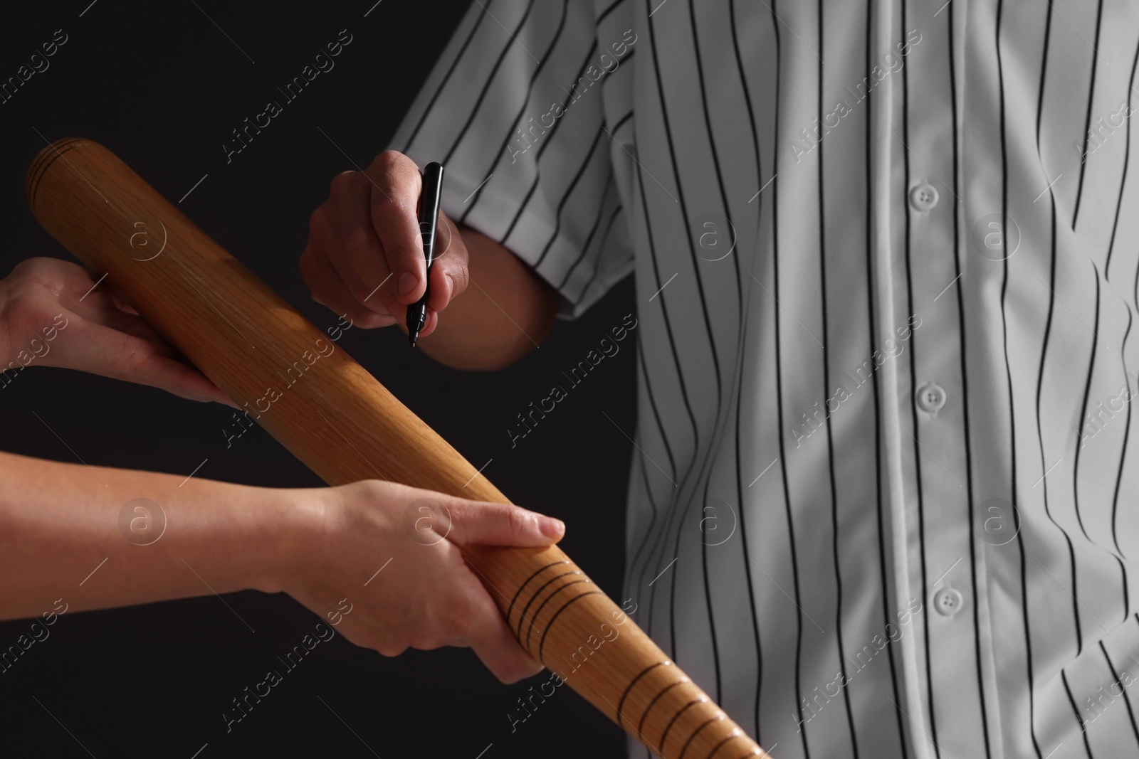 Photo of Baseball player signing autograph on bat against black background, closeup