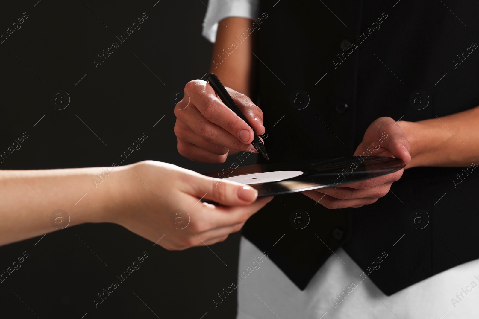 Photo of Singer signing autograph on vinyl record against black background, closeup