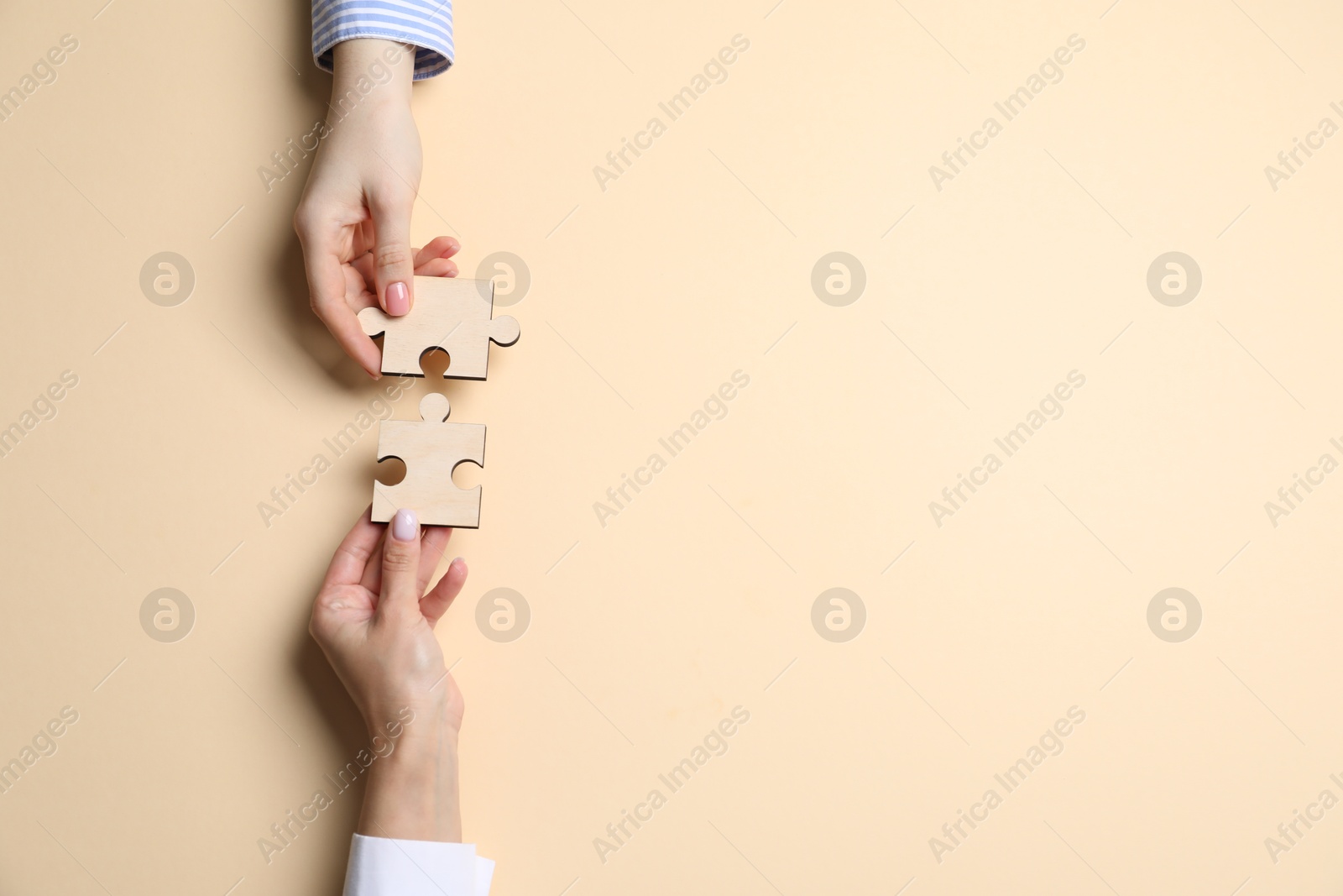 Photo of Business strategy and teamwork concept. Partners putting puzzle pieces together on beige background, top view. Space for text