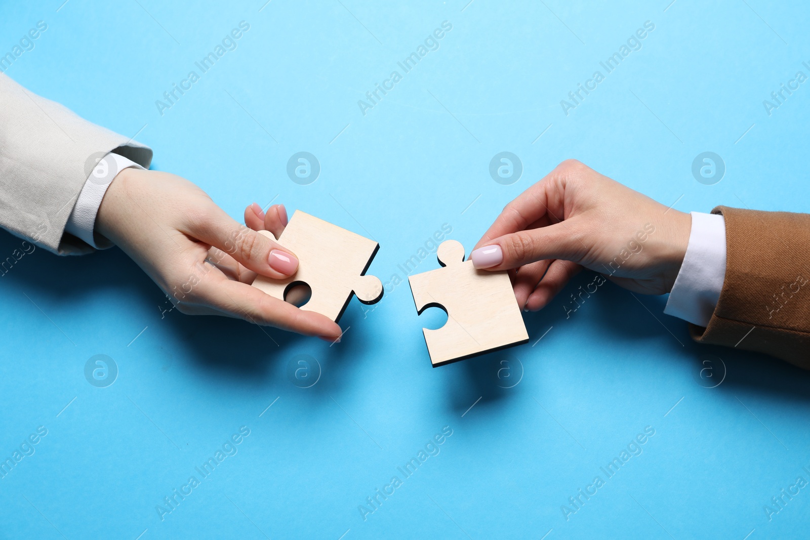 Photo of Business strategy and teamwork concept. Partners putting puzzle pieces together on light blue background, top view