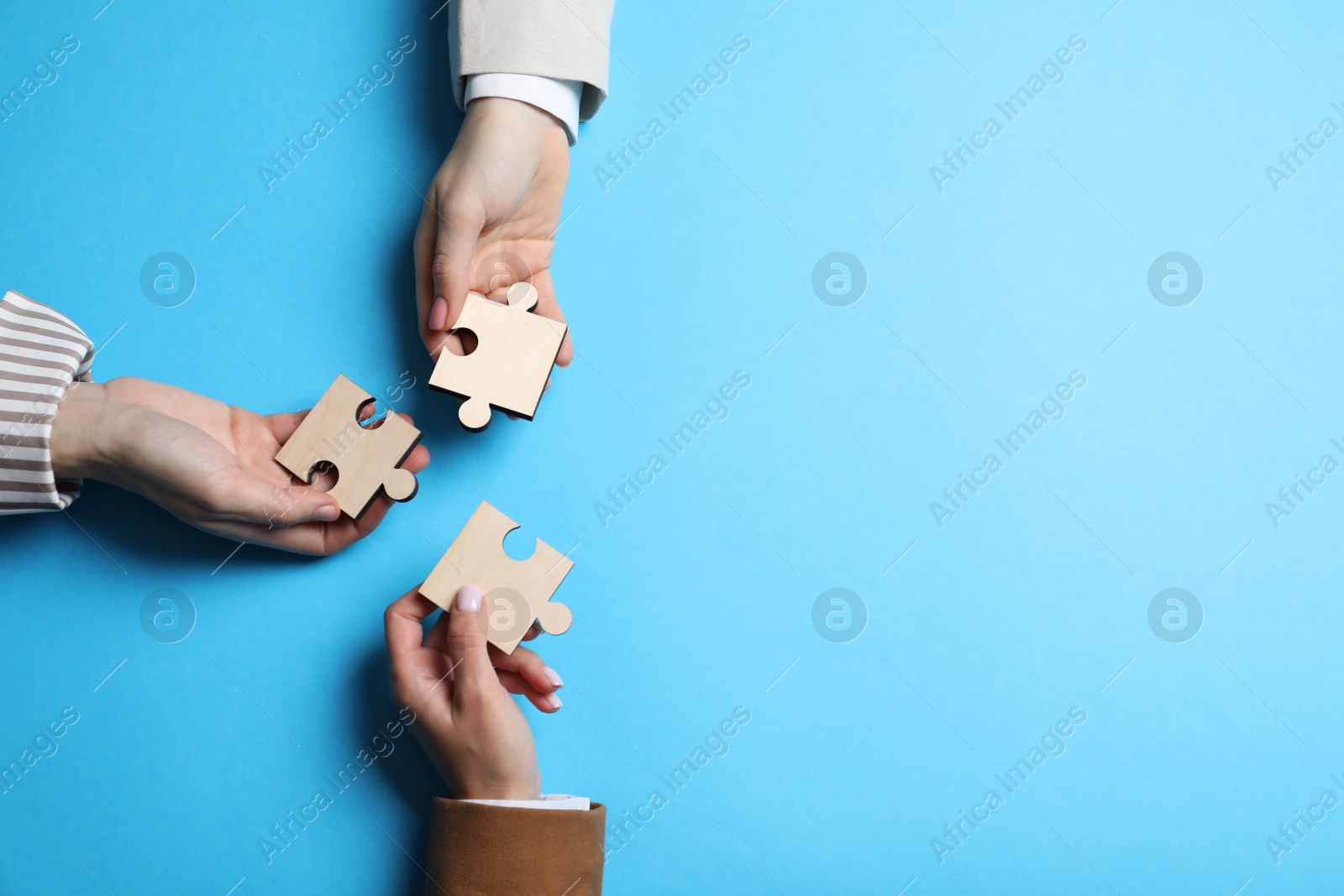 Photo of Business strategy and teamwork concept. Partners with different puzzle pieces on light blue background, top view. Space for text