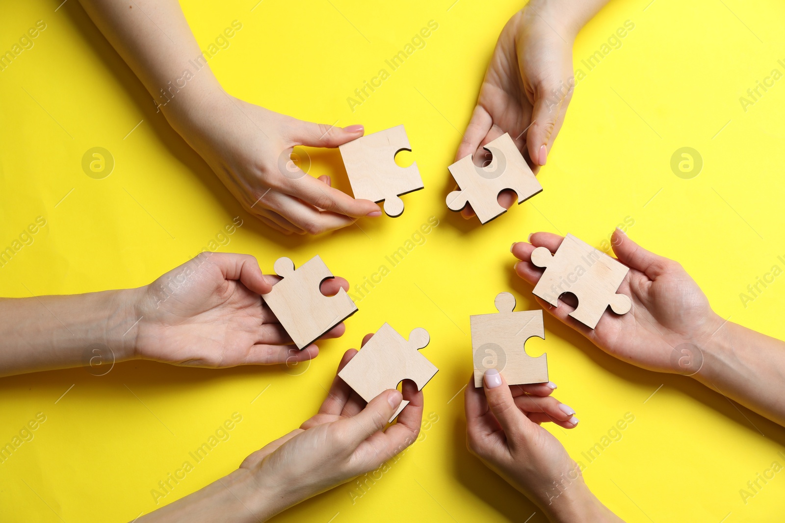 Photo of Business strategy and teamwork concept. Group of businesspeople with different puzzle pieces on yellow background, top view