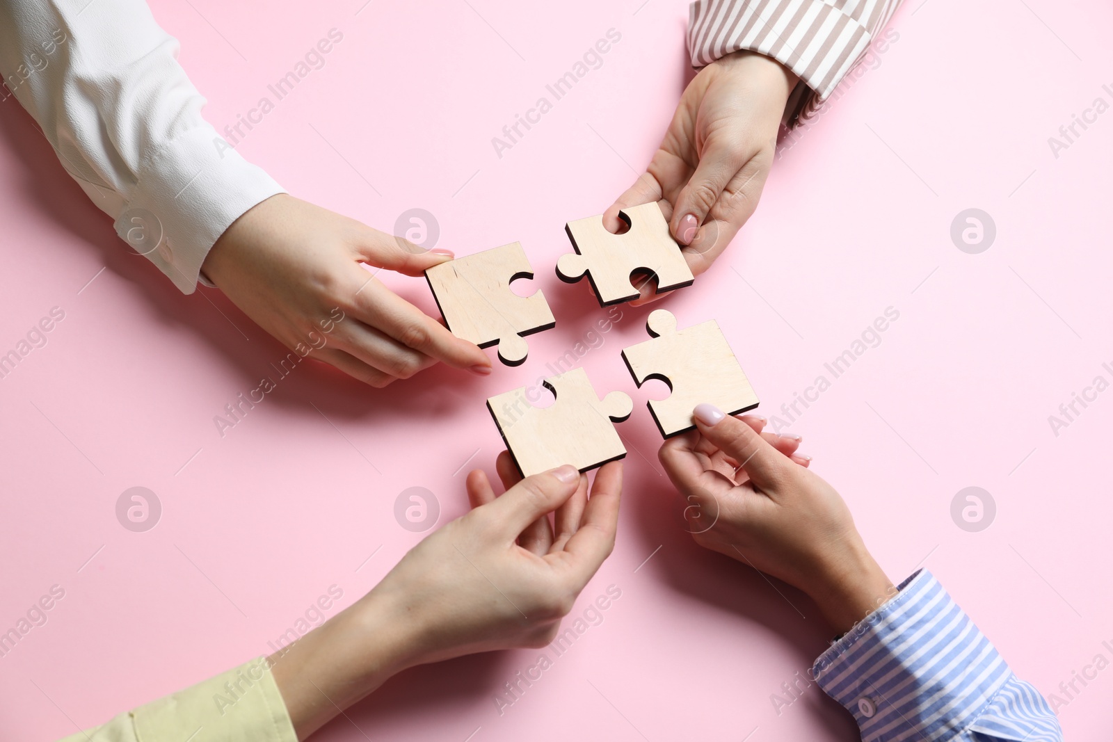 Photo of Business strategy and teamwork concept. Group of businesspeople putting puzzle pieces together on pink background, above view