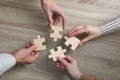 Photo of Teamwork. Group of people putting puzzle pieces together at wooden table, top view