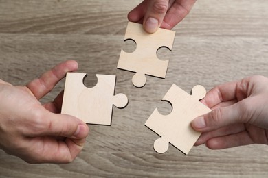 Photo of Teamwork. People putting puzzle pieces together at wooden table, top view