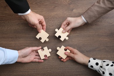 Photo of Teamwork. Group of people putting puzzle pieces together at wooden table, top view