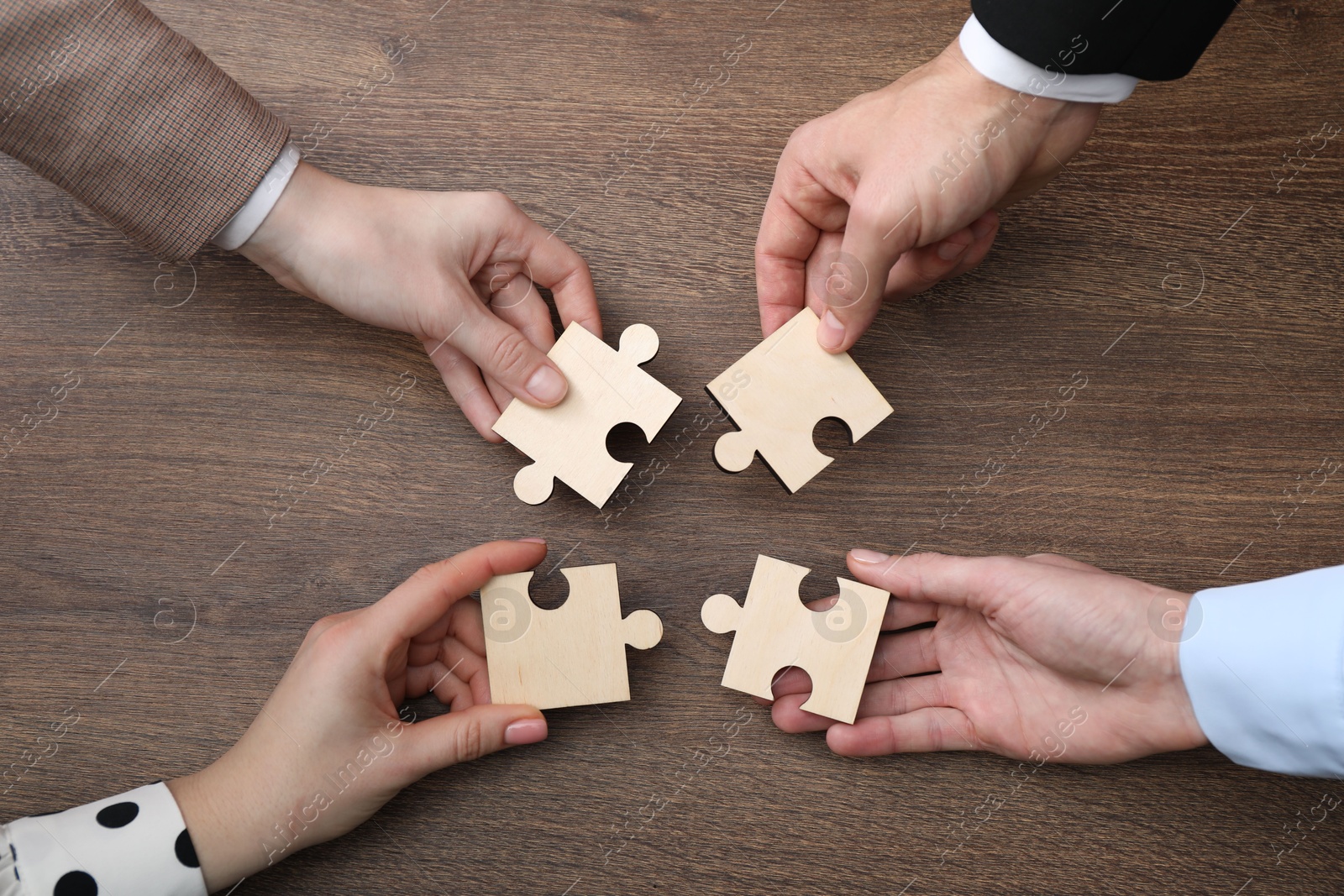 Photo of Teamwork. Group of people putting puzzle pieces together at wooden table, top view