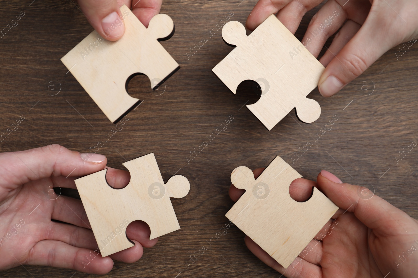 Photo of Teamwork. Group of people putting puzzle pieces together at wooden table, top view