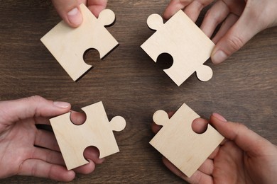 Photo of Teamwork. Group of people putting puzzle pieces together at wooden table, top view