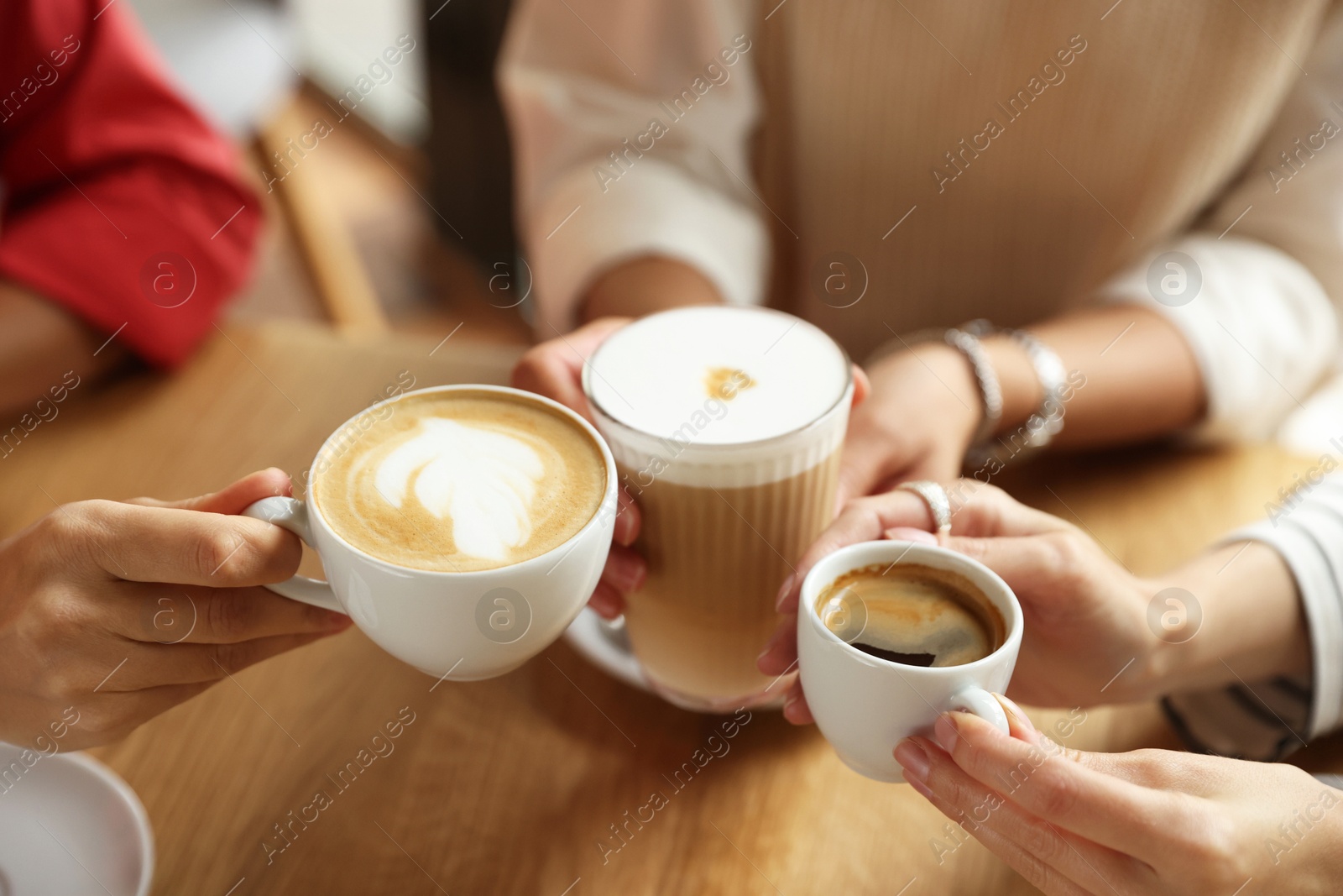 Photo of Women with cups of delicious coffee drinks at wooden table in cafe, closeup