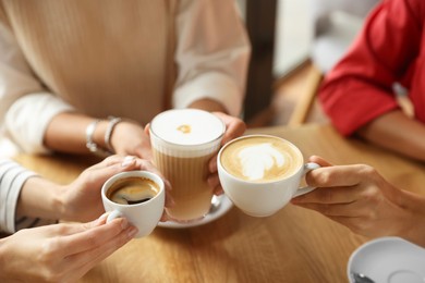 Photo of Women with cups of delicious coffee drinks at wooden table in cafe, closeup