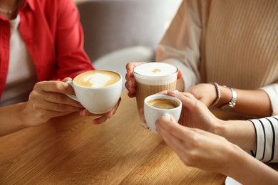 Photo of Women with cups of delicious coffee drinks at wooden table in cafe, closeup