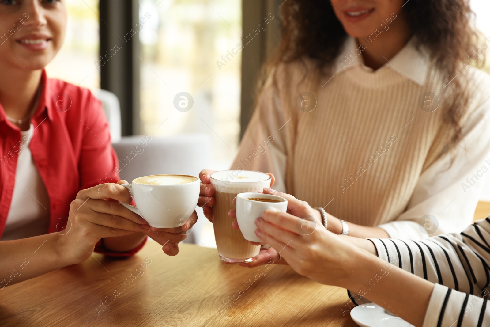 Photo of Women with cups of delicious coffee drinks at wooden table in cafe, closeup