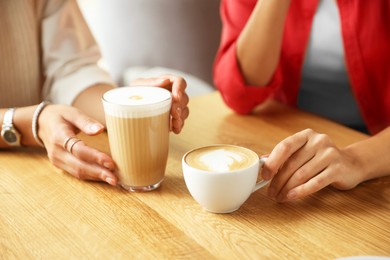 Photo of Women with cups of delicious coffee drinks at wooden table in cafe, closeup