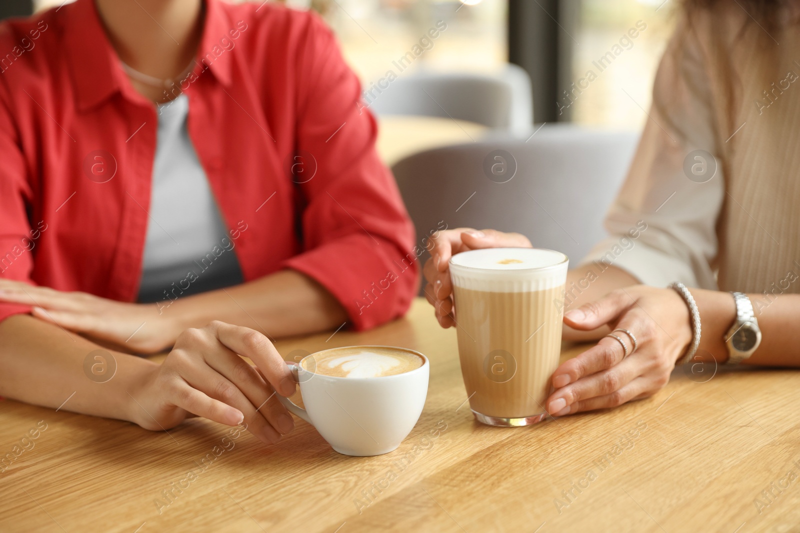 Photo of Women with cups of delicious coffee drinks at wooden table in cafe, closeup