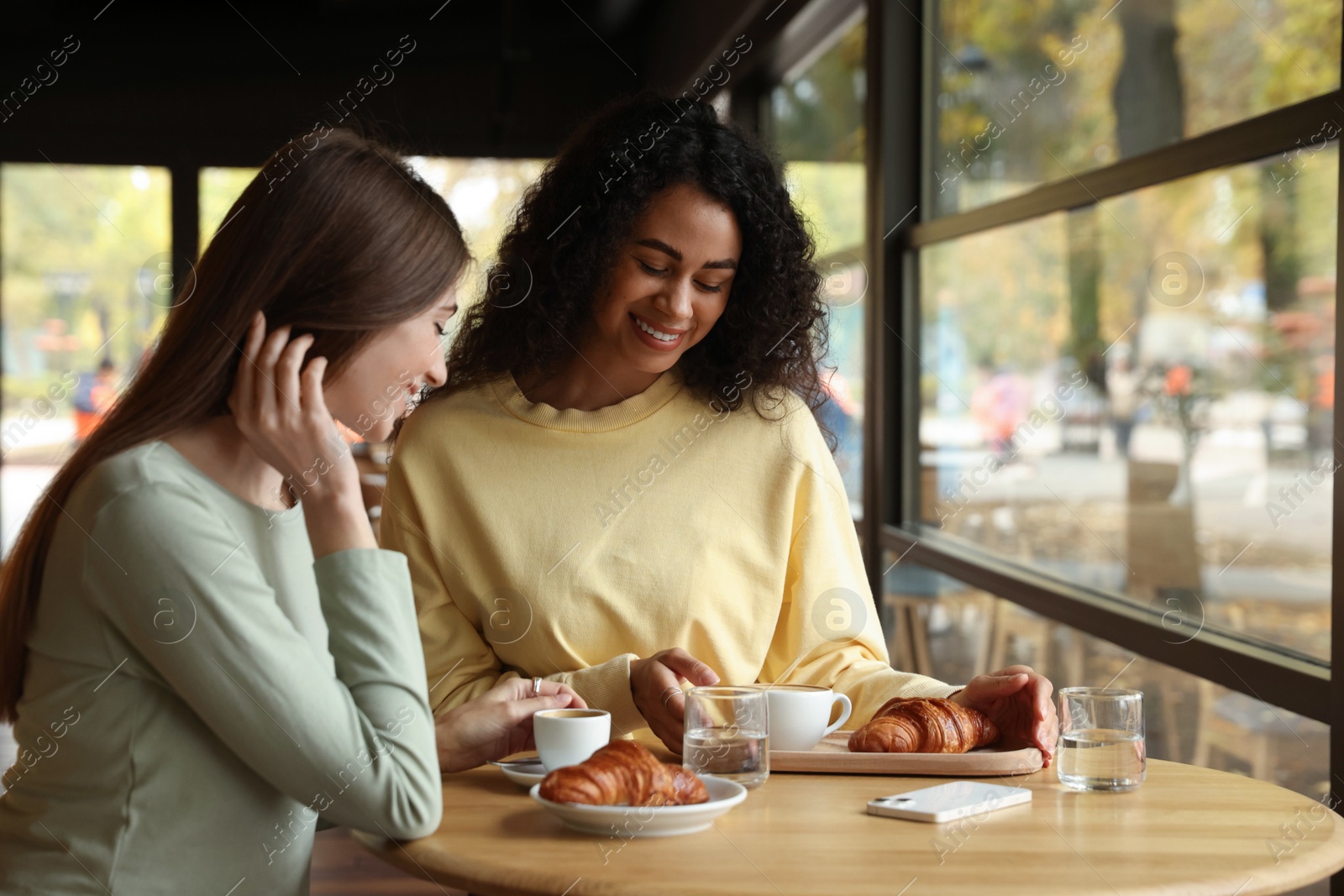 Photo of Happy women with coffee drinks chatting in cafe