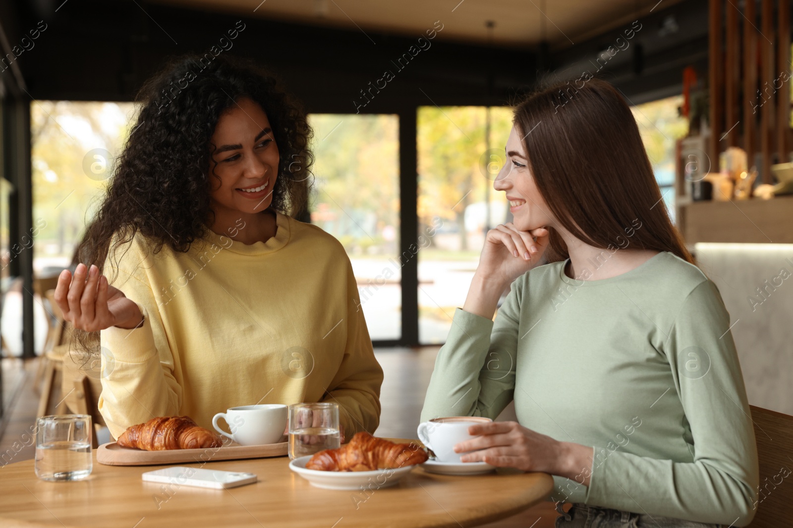 Photo of Happy women with coffee drinks chatting in cafe