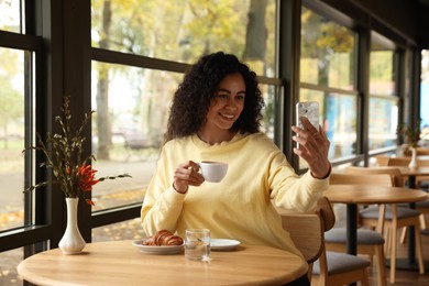 Photo of Woman with cup of coffee taking selfie in cafe