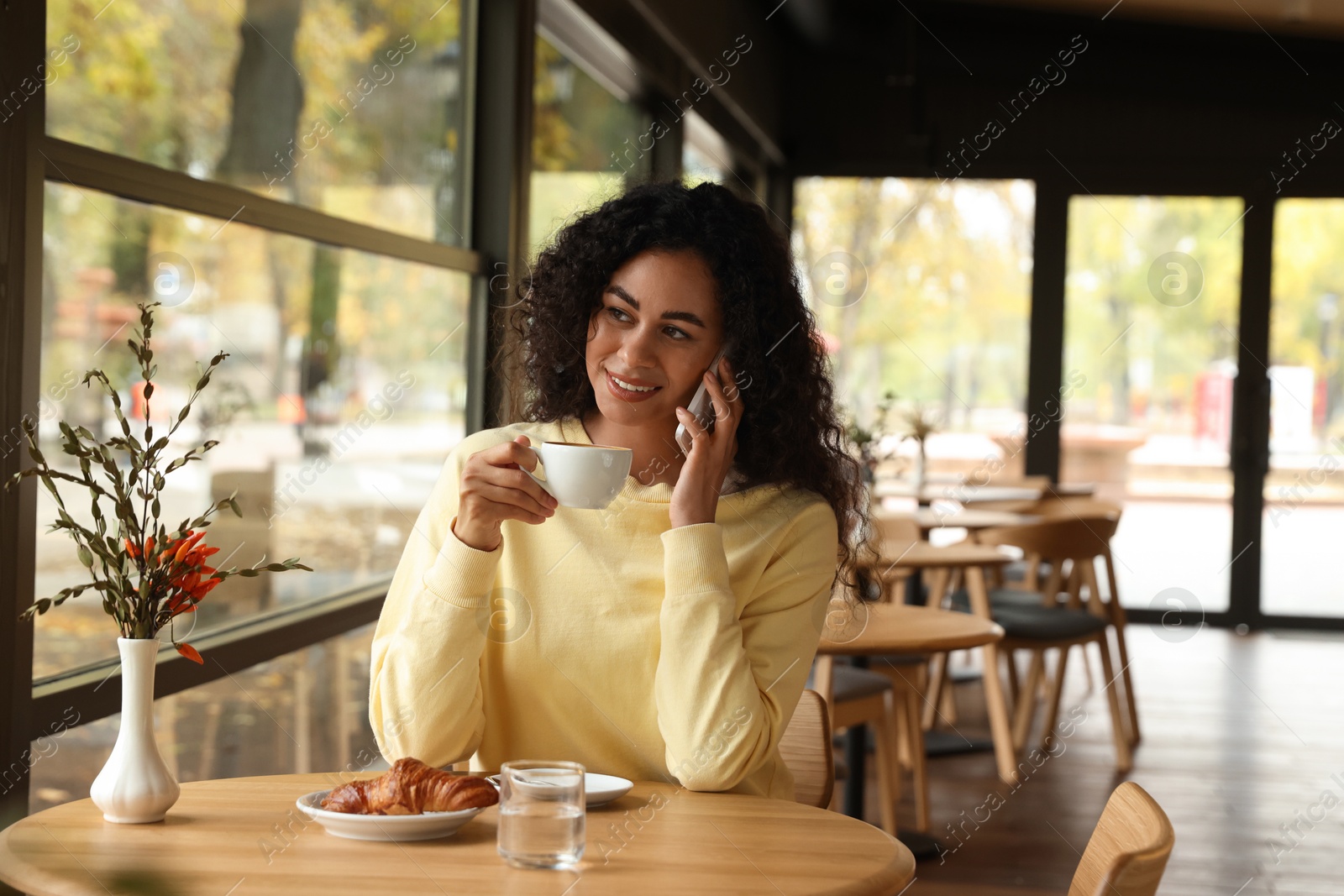 Photo of Woman with cup of coffee talking on phone in cafe