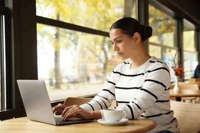 Photo of Woman working on laptop at table in cafe