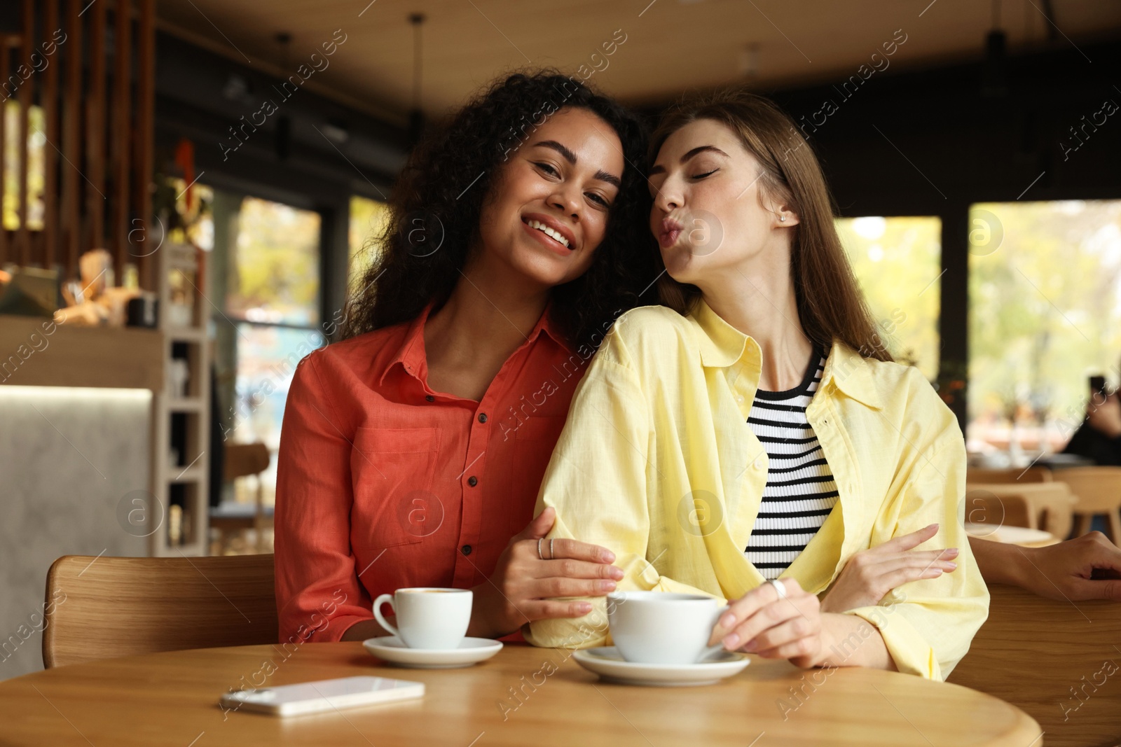 Photo of Happy women with coffee drinks at table in cafe