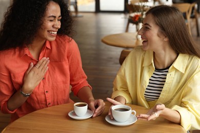 Photo of Happy women with coffee drinks chatting in cafe