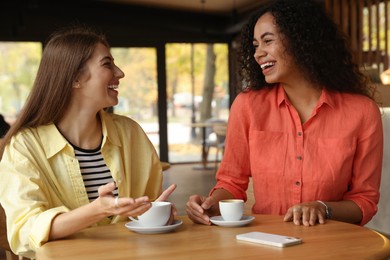 Photo of Happy women with coffee drinks chatting in cafe