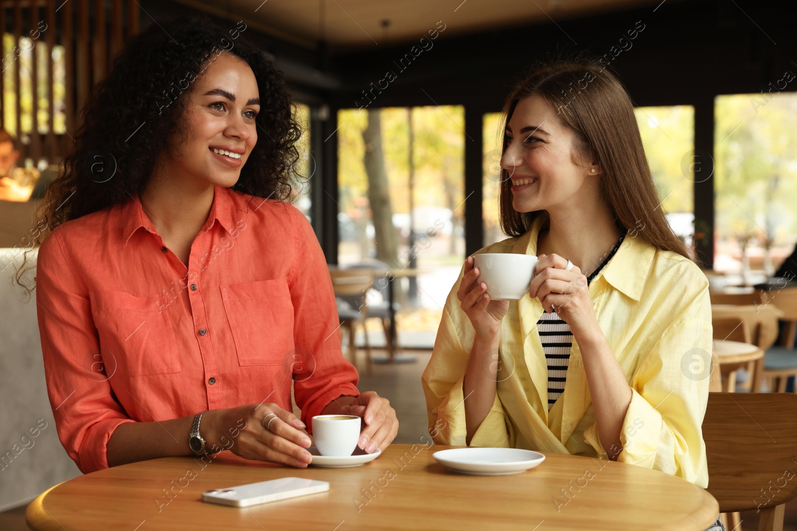 Photo of Happy women with coffee drinks chatting in cafe