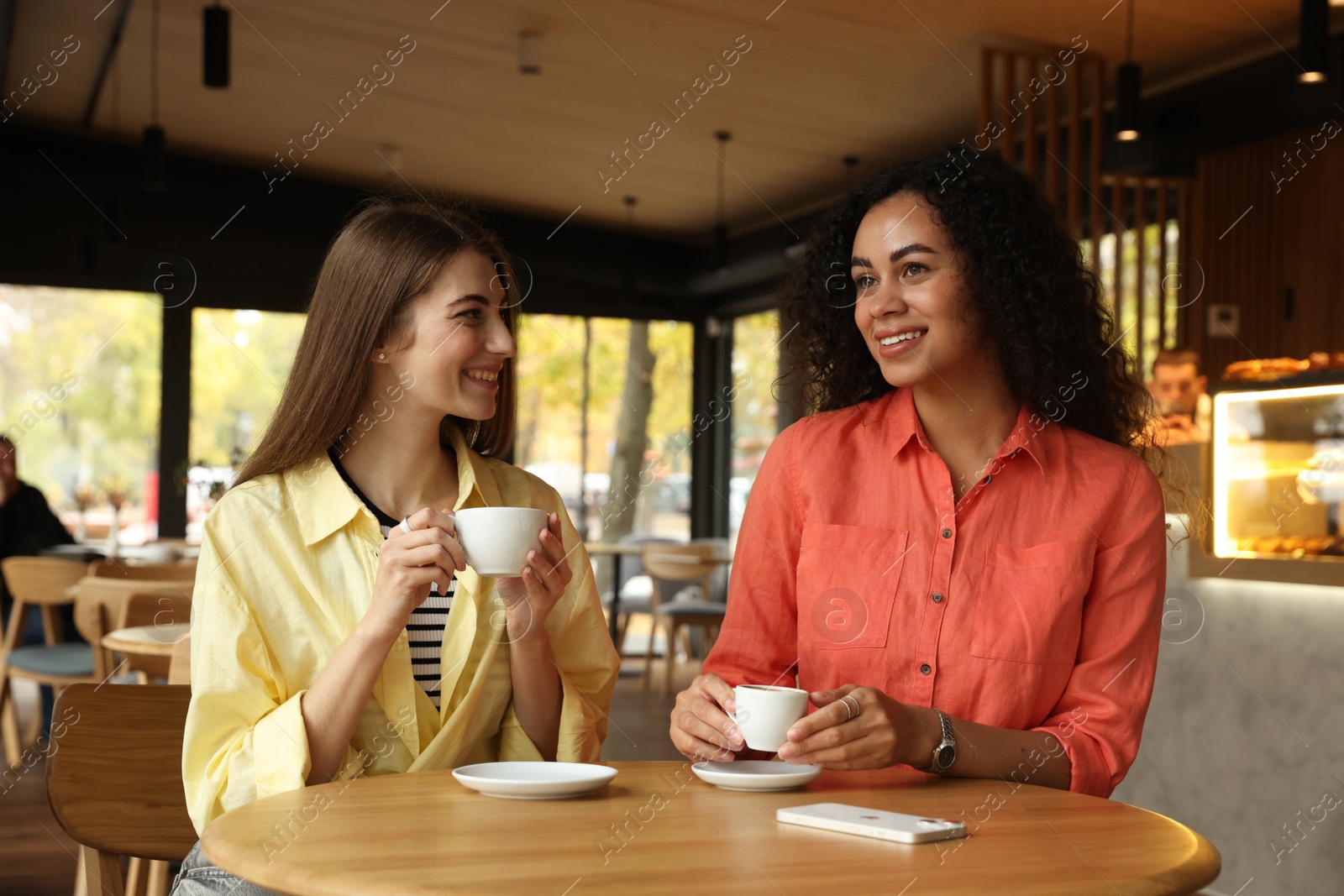 Photo of Happy women with coffee drinks at table in cafe