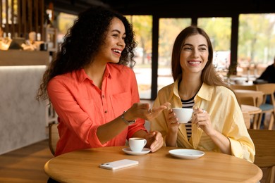 Photo of Happy women with coffee drinks chatting in cafe